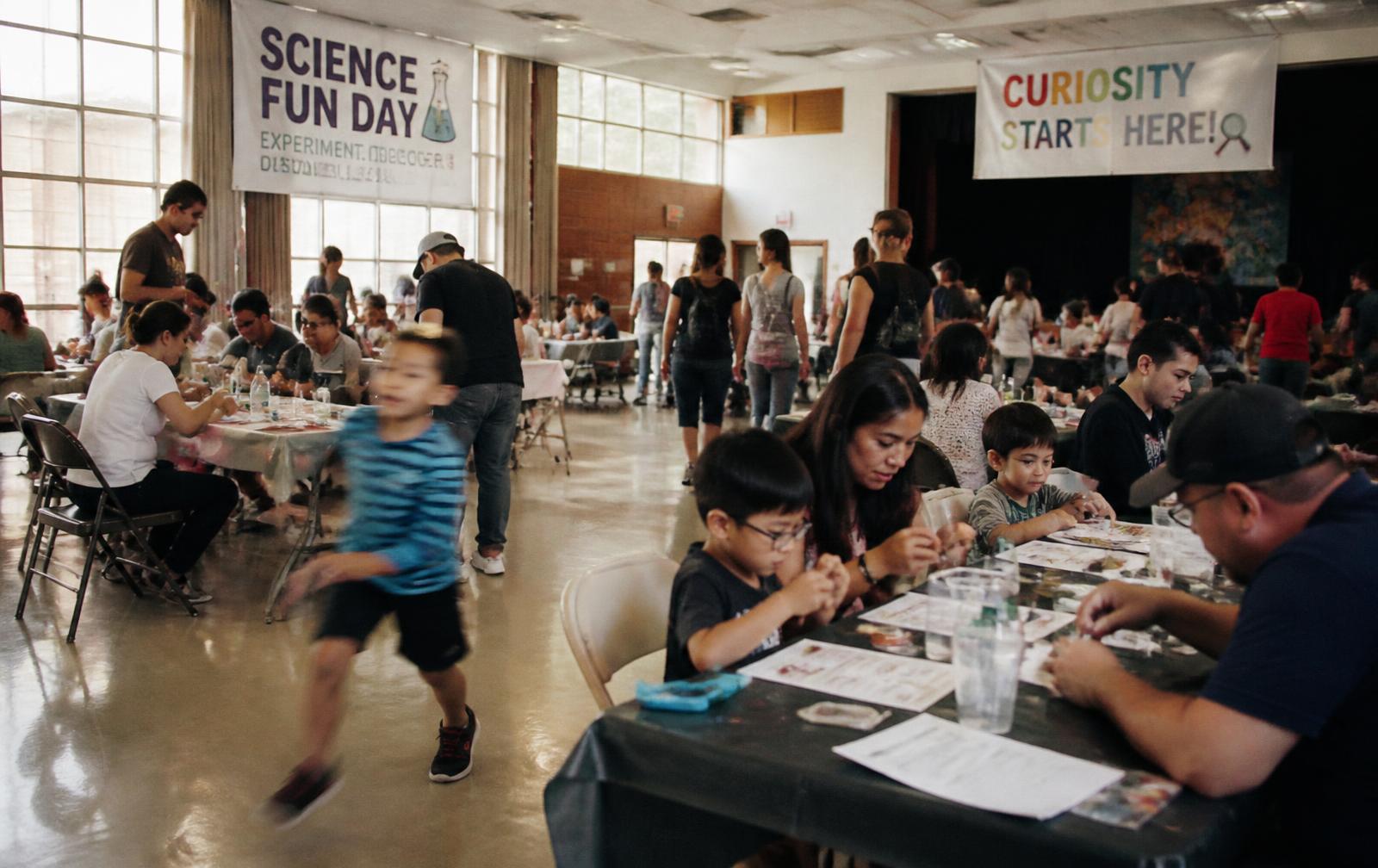 Children and families gathered around a table of maker projects at a curiosity event