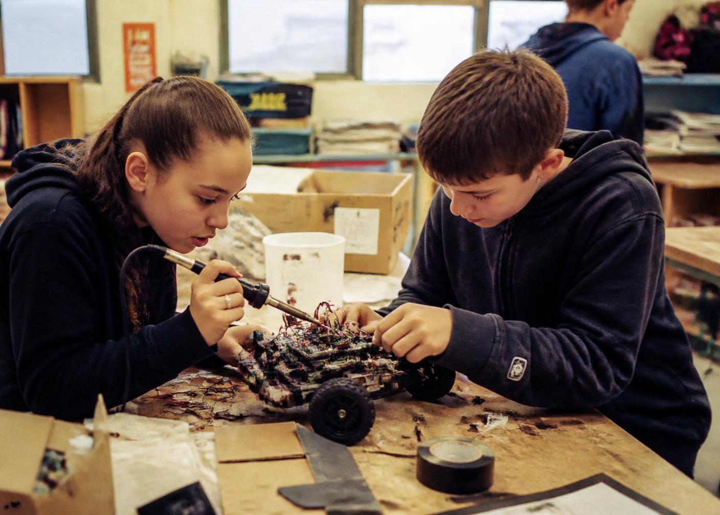 A child's hands assembling a colourful invention from recycled parts